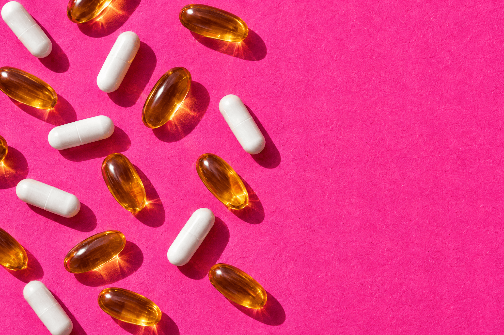 Amber softgels and white capsules scattered on pink paper.